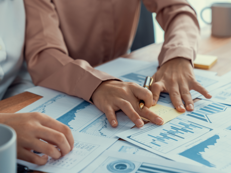 two hands holding a pen, looking over statistics and graphs