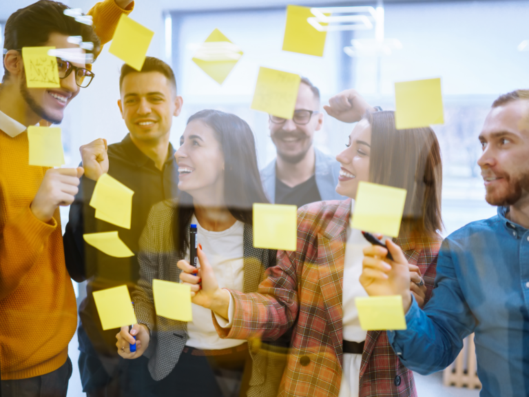 A group of people brainstorming at a glass window with yellow post its