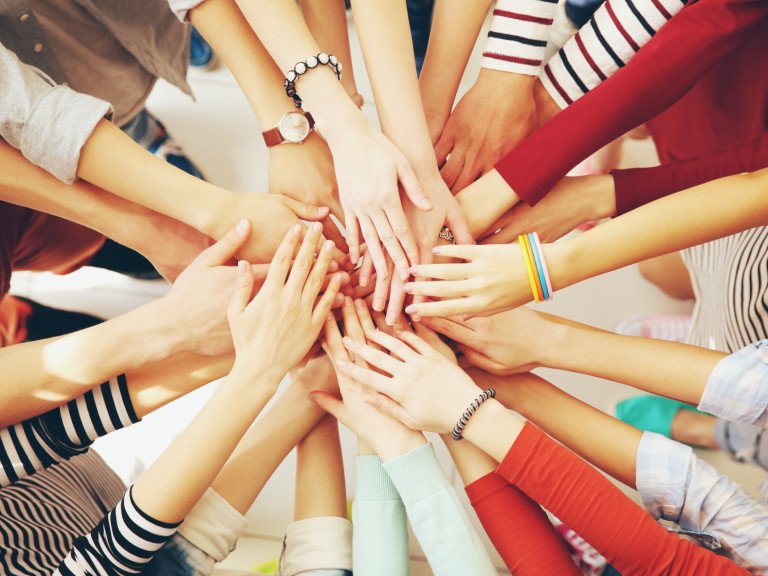 People's hands all reaching into the centre of a group