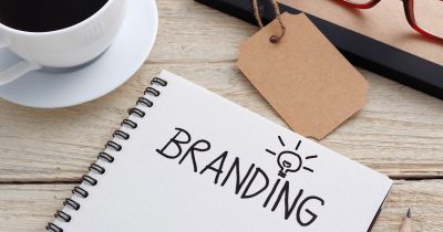 note book with the word 'branding' written in capital letters with a lightbulb. a cup of coffee and glasses