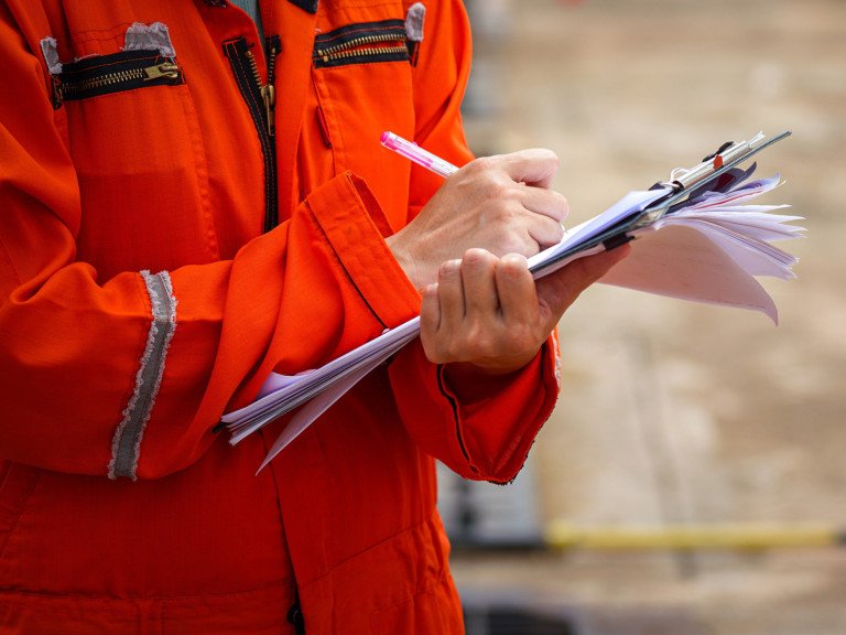 Person wearing high vis clothing writing on paper with a clipboard