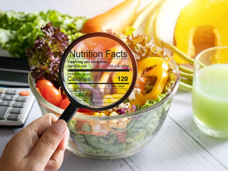 nutritional information concept. hand use the magnifying glass to zoom in to see the details of the nutrition facts from food , salad bowl