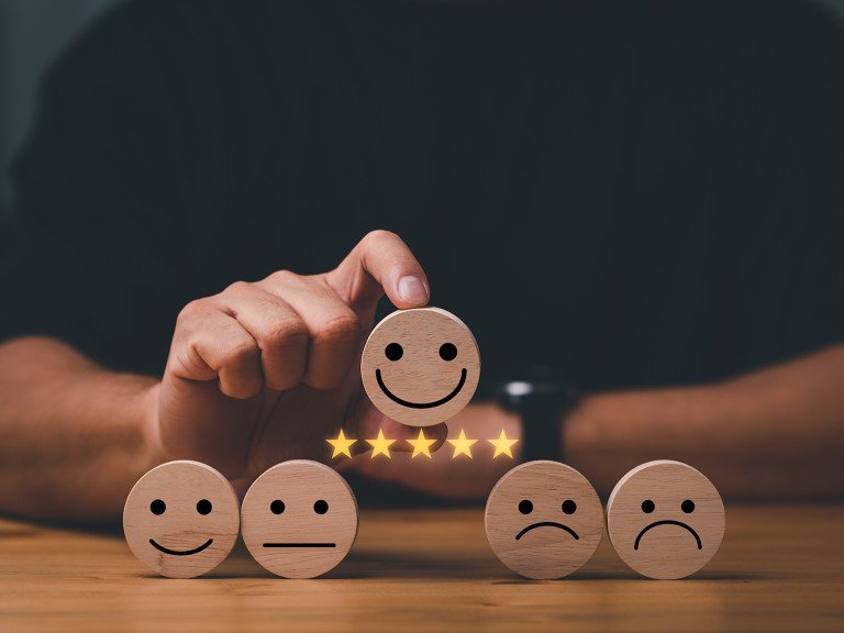 5 wooden circles with faces on them, ranging from sad to happy, with someone holding the happiest face