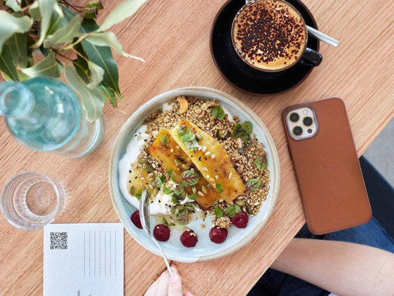 birds eye view of a table with a breakfast dish, a coffee, water and a phone
