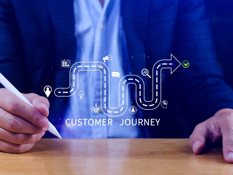 Close up of man holding pen at a desk with a virtual customer journey displayed above the desk.