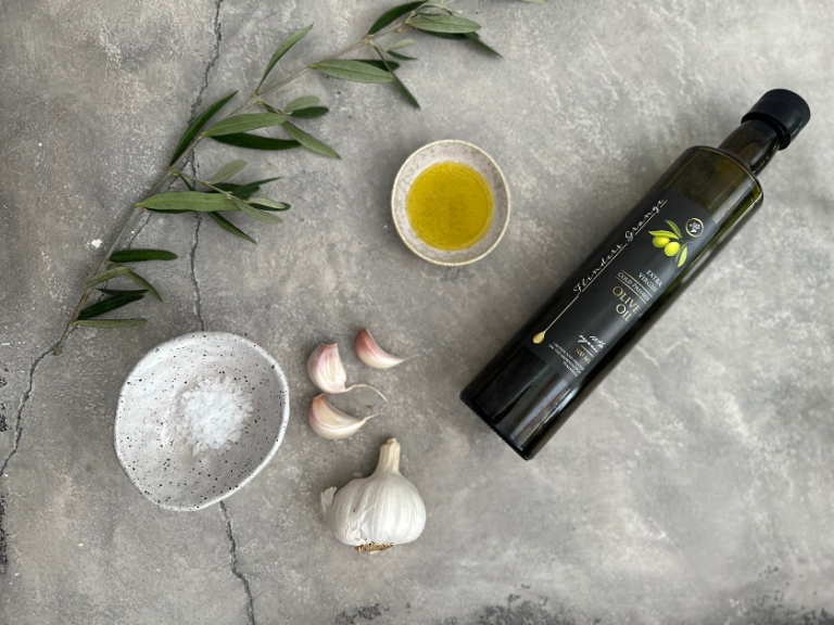 A flatlay photo of olive oil, garlic, foliage on a table